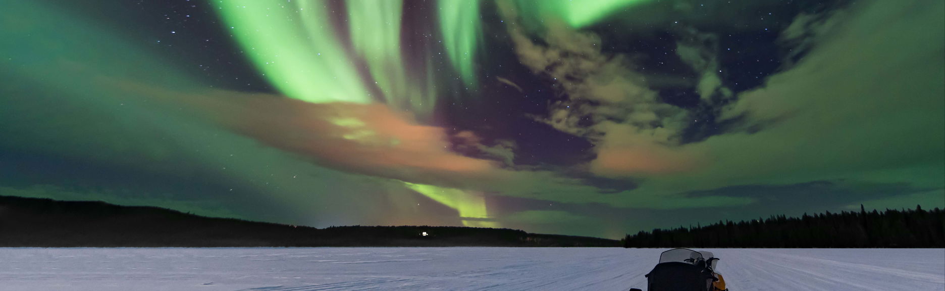 Passeio de moto de neve sob a aurora boreal